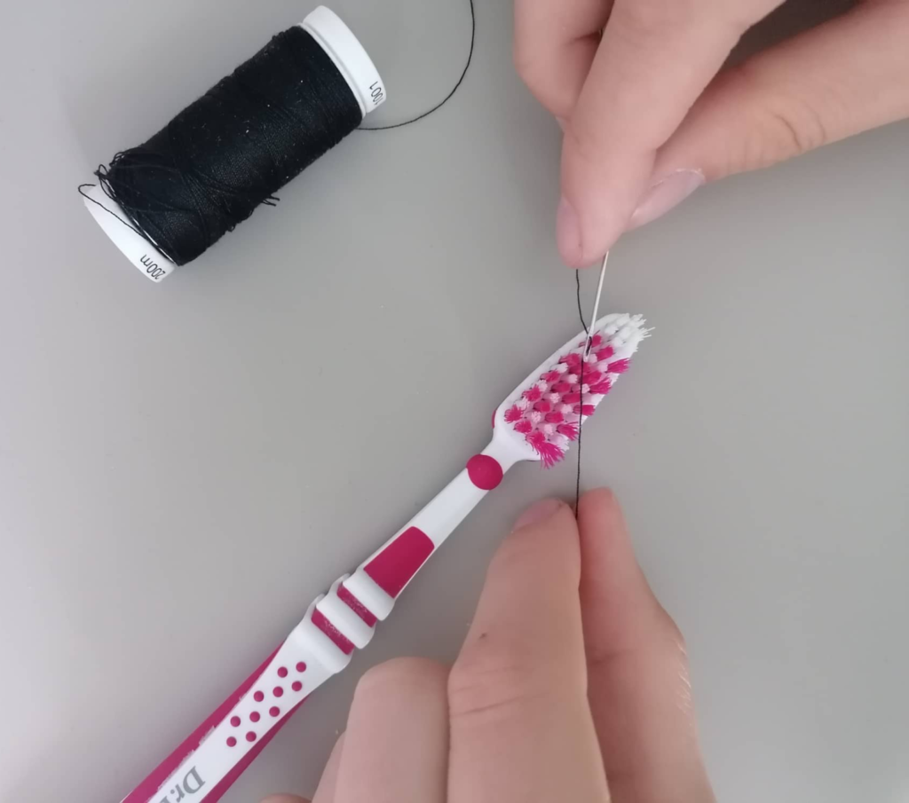 歯ブラシを使って針に糸を通す方法を説明している写真です。歯ブラシのブラシに斜めに糸と針が置かれています。